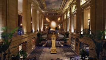 Un'ampia hall d'albergo con una scalinata centrale, colonne decorate e un soffitto ornamentale.