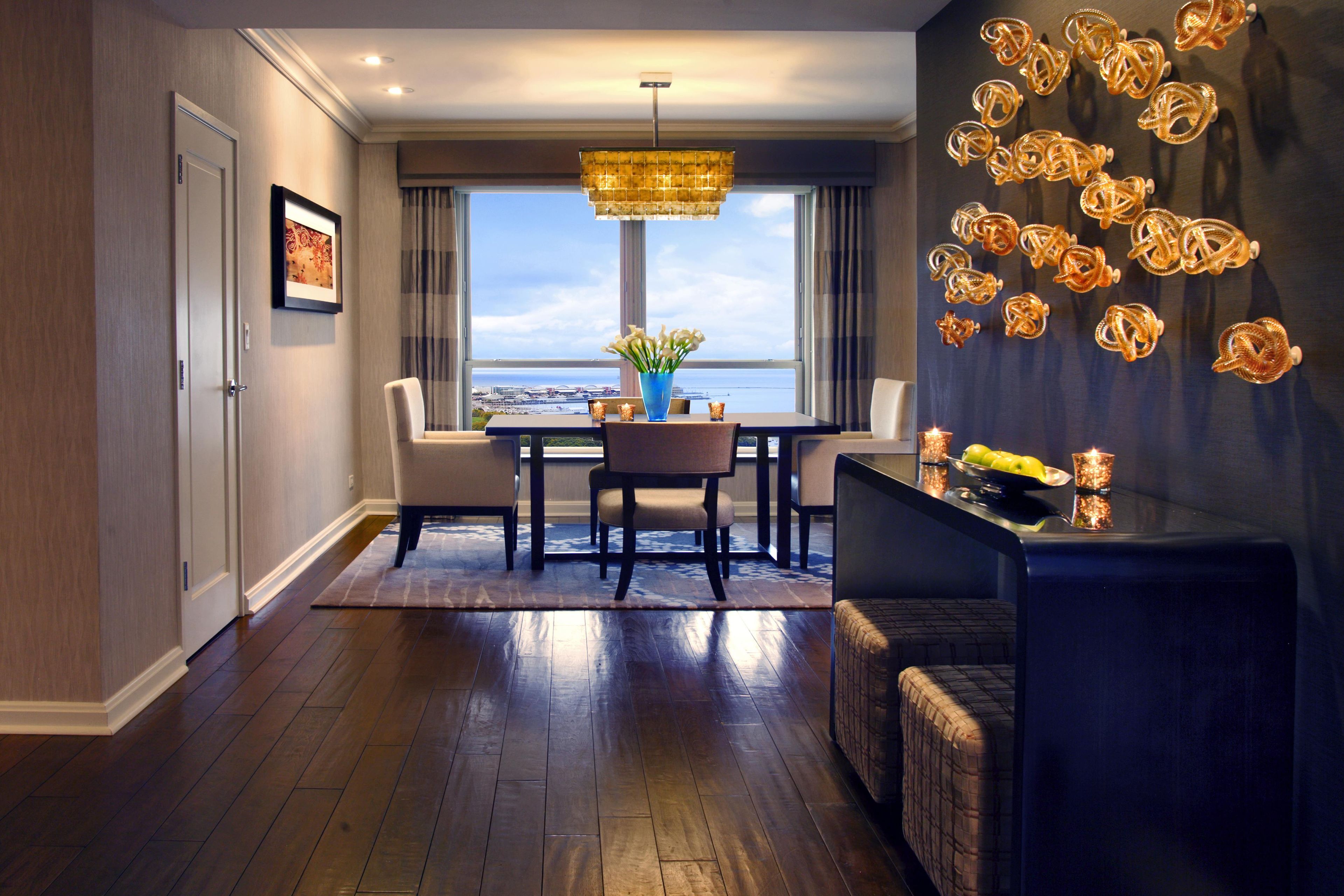 A modern hotel room with a dining area, a view of the cityscape, and a decorative wall with golden ornaments.