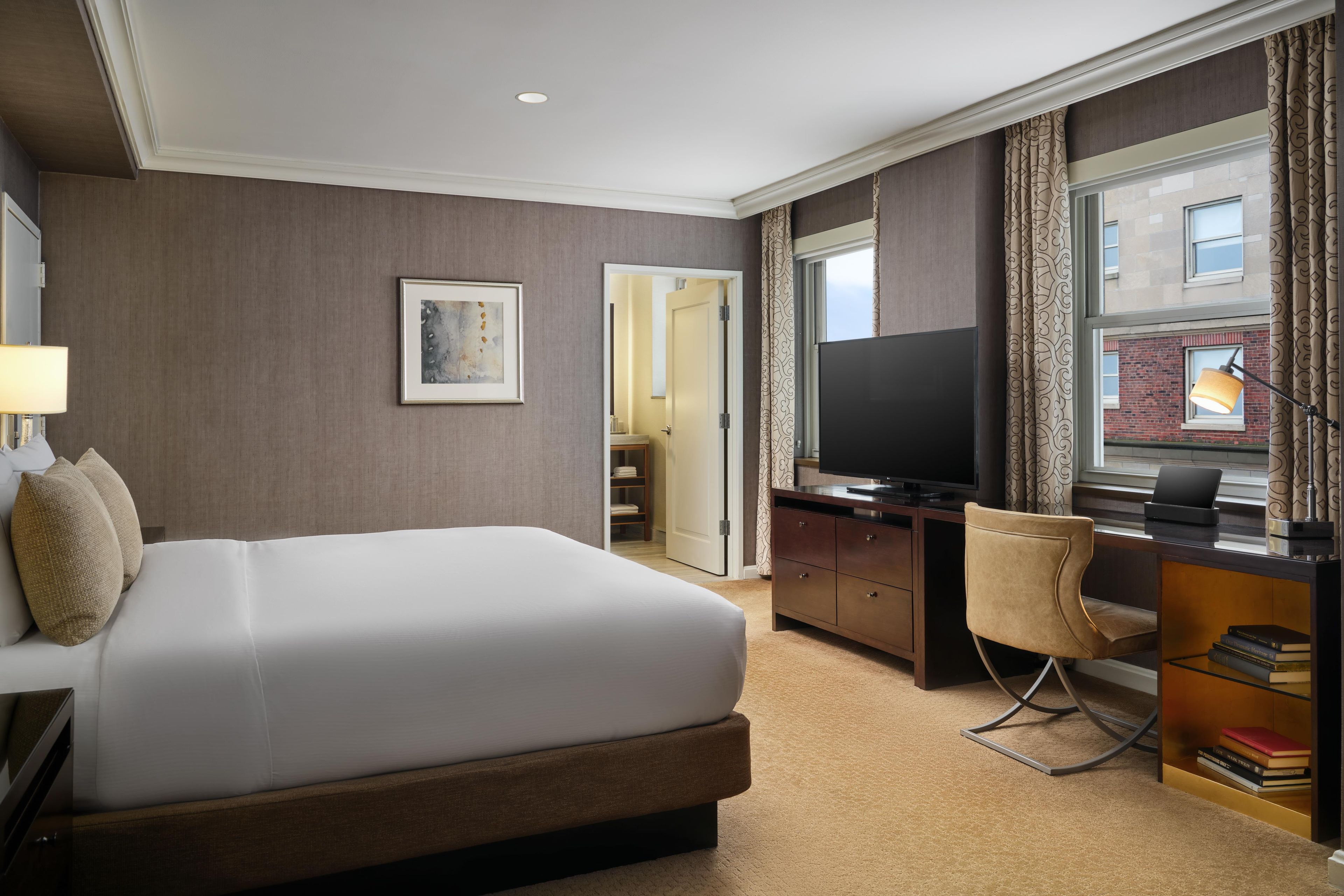 A hotel room with a bed, desk, chair, TV, and a window with curtains.