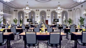 A hotel dining area with multiple tables, chairs, chandeliers, and a large screen displaying the Hilton logo.
