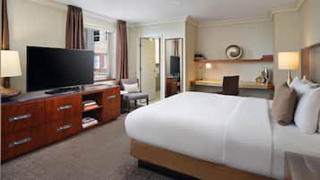 A hotel room with a large bed, a TV, a desk with a chair, and a bookshelf.