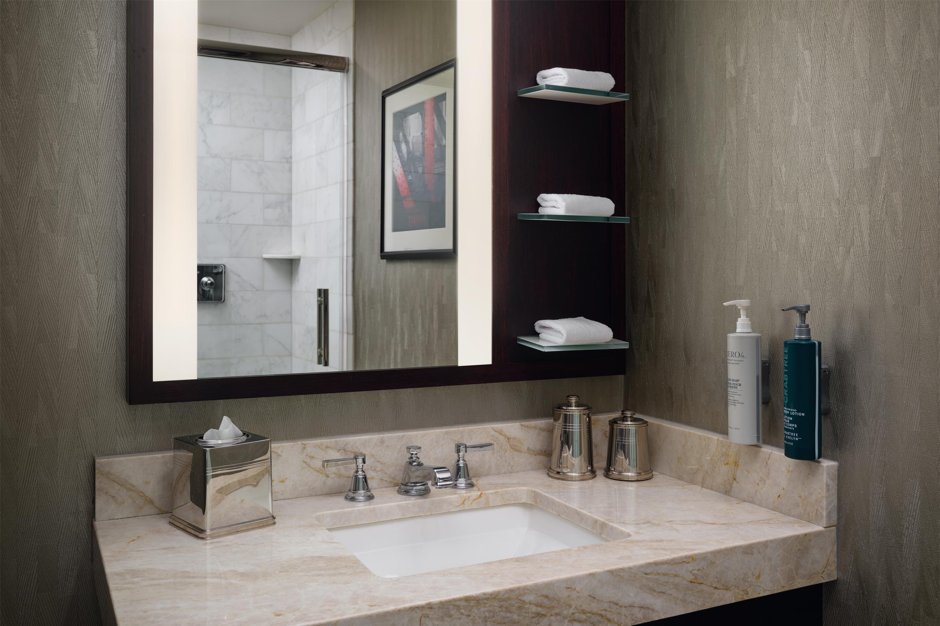 A bathroom with a marble sink, a large mirror, and shelves with toiletries.