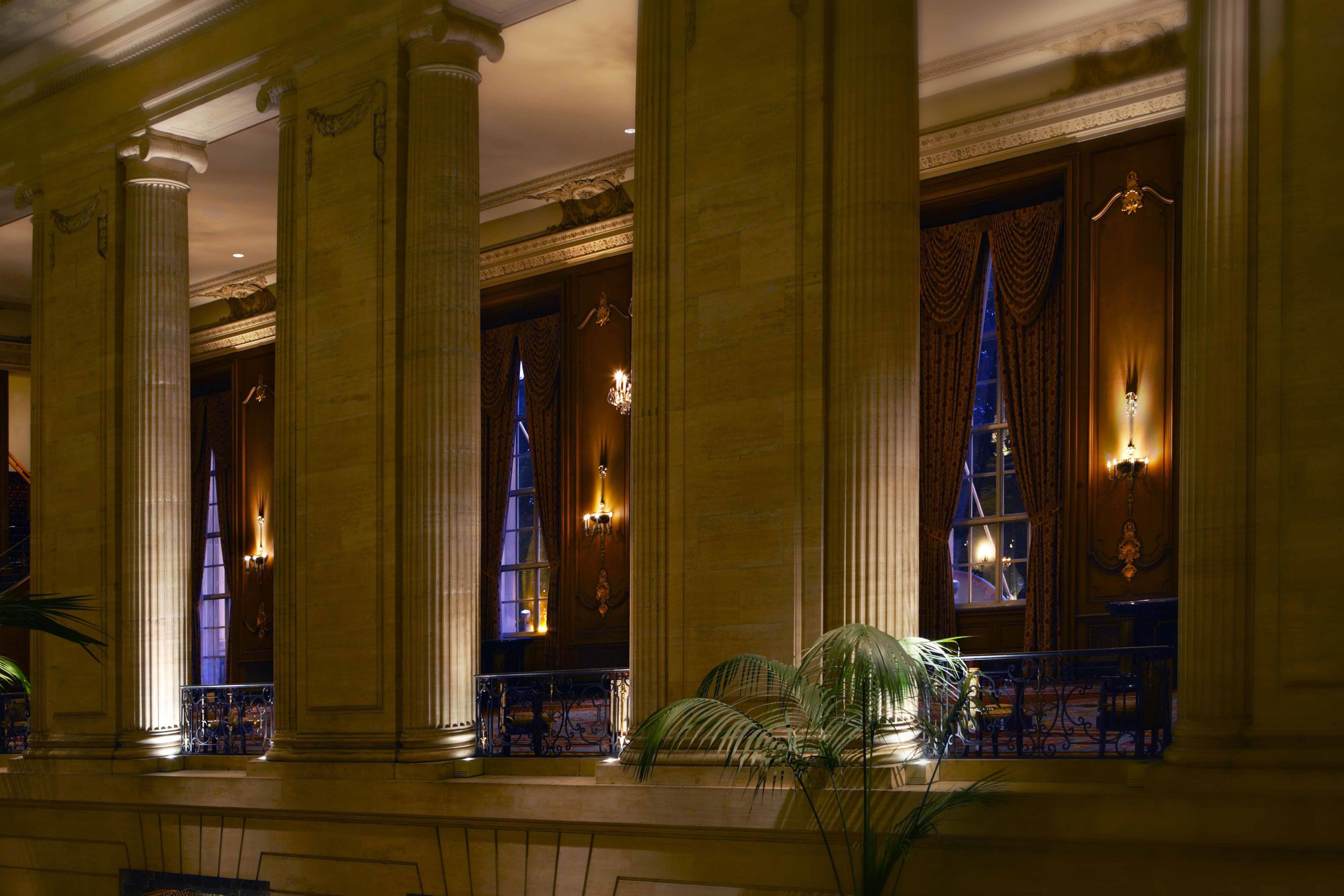 A grand lobby with large columns, ornate chandeliers, and a staircase leading to an upper level.