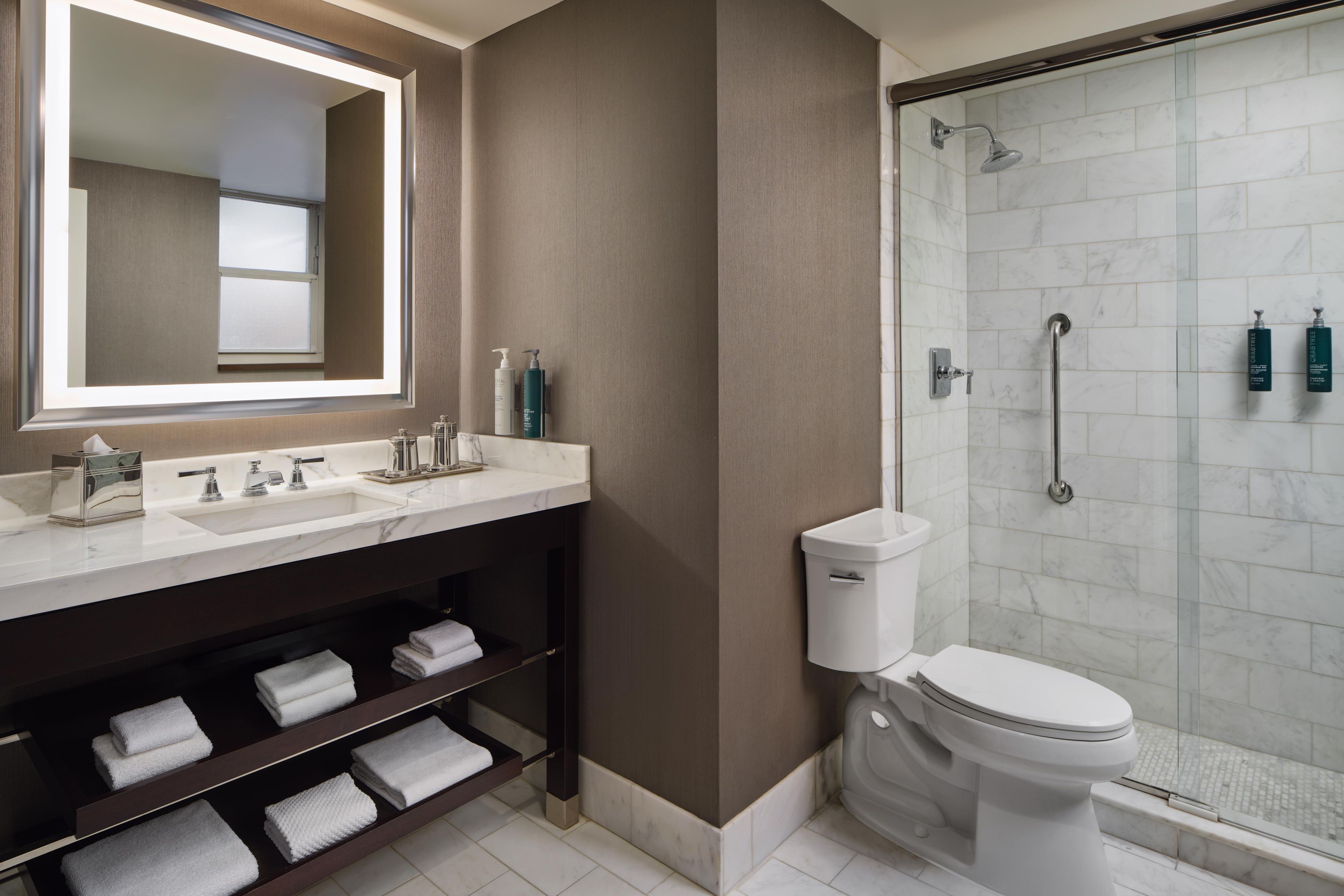 A modern bathroom with a large mirror, two sinks, a toilet, and a glass-enclosed shower.
