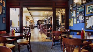 Un interior de restaurante con mesas y sillas de madera, piso alfombrado y cuadros en las paredes.