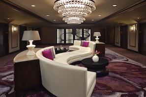Un hall d’hôtel moderne avec un canapé blanc incurvé, deux tables d’appoint avec des lampes, une table basse noire et un grand lustre.