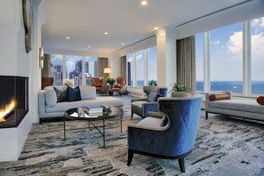 A modern living room with a fireplace, sofas, armchairs, a coffee table, and large windows offering a city view.