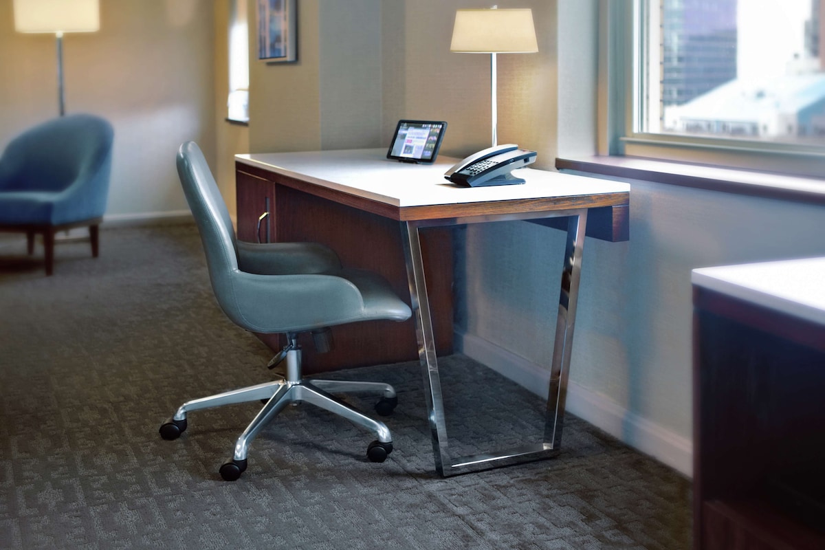 A hotel room with a desk, chair, lamp, and a tablet.