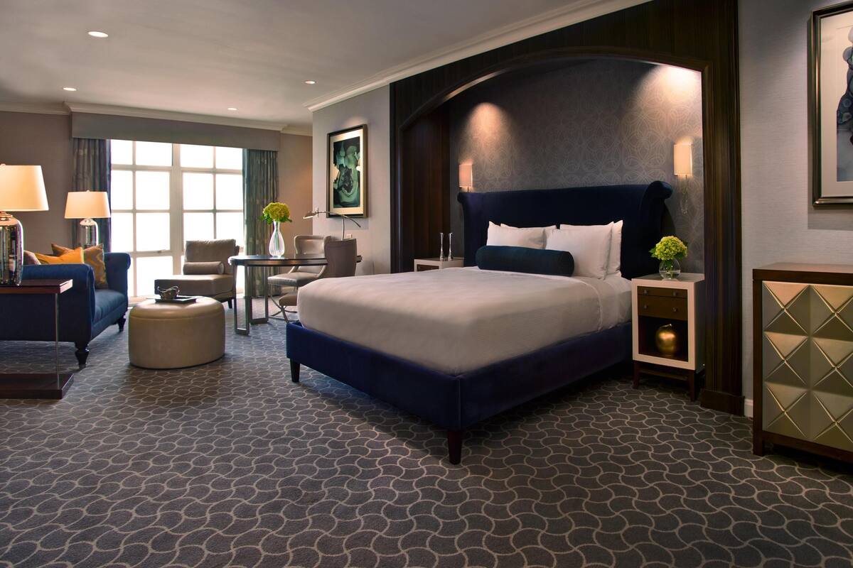 Una habitación de hotel con una cama grande, un escritorio, una silla, una lámpara y un jarrón con flores.