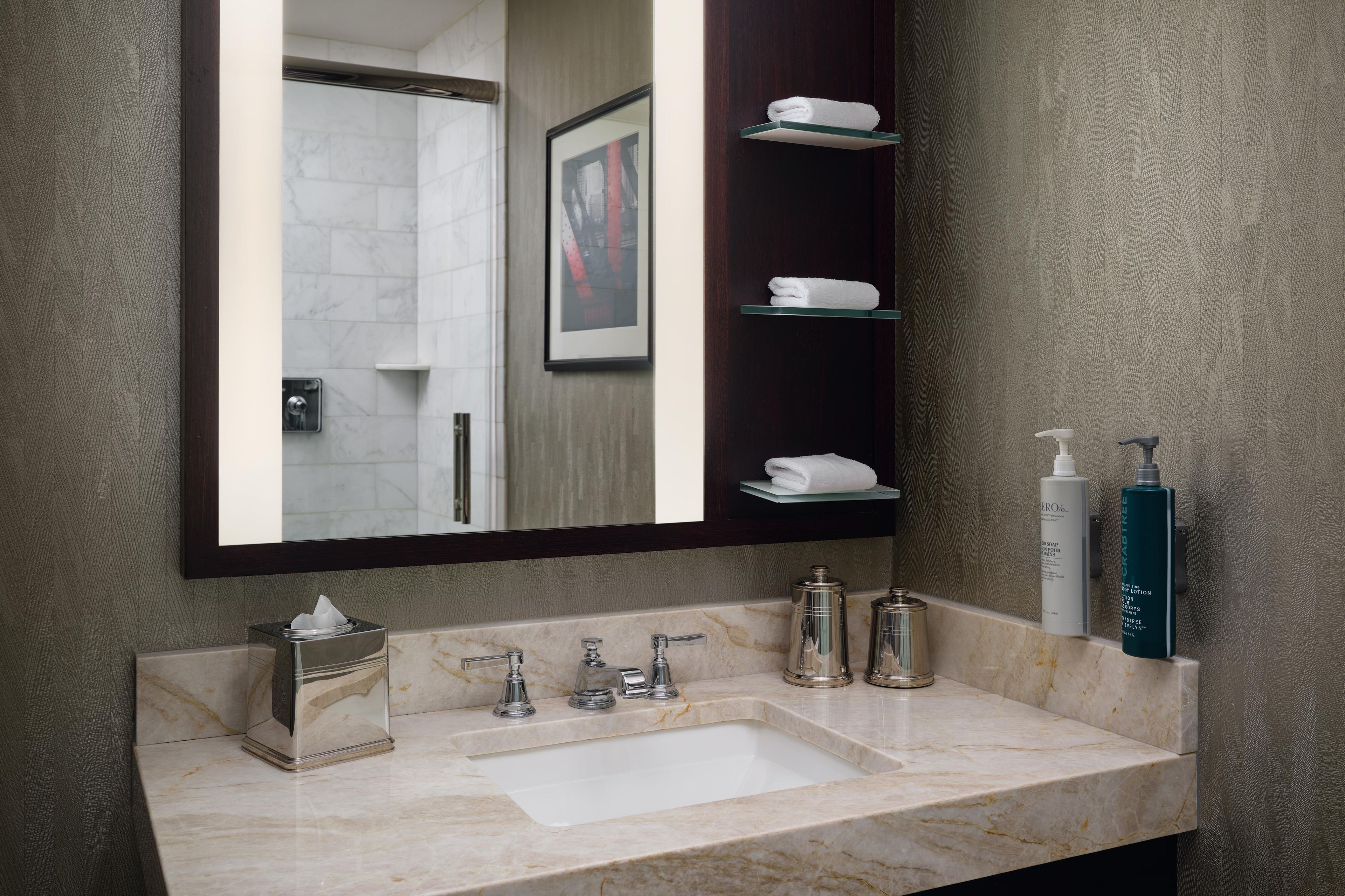 Baño con lavamanos de mármol, espejo, toallero y artículos de aseo.