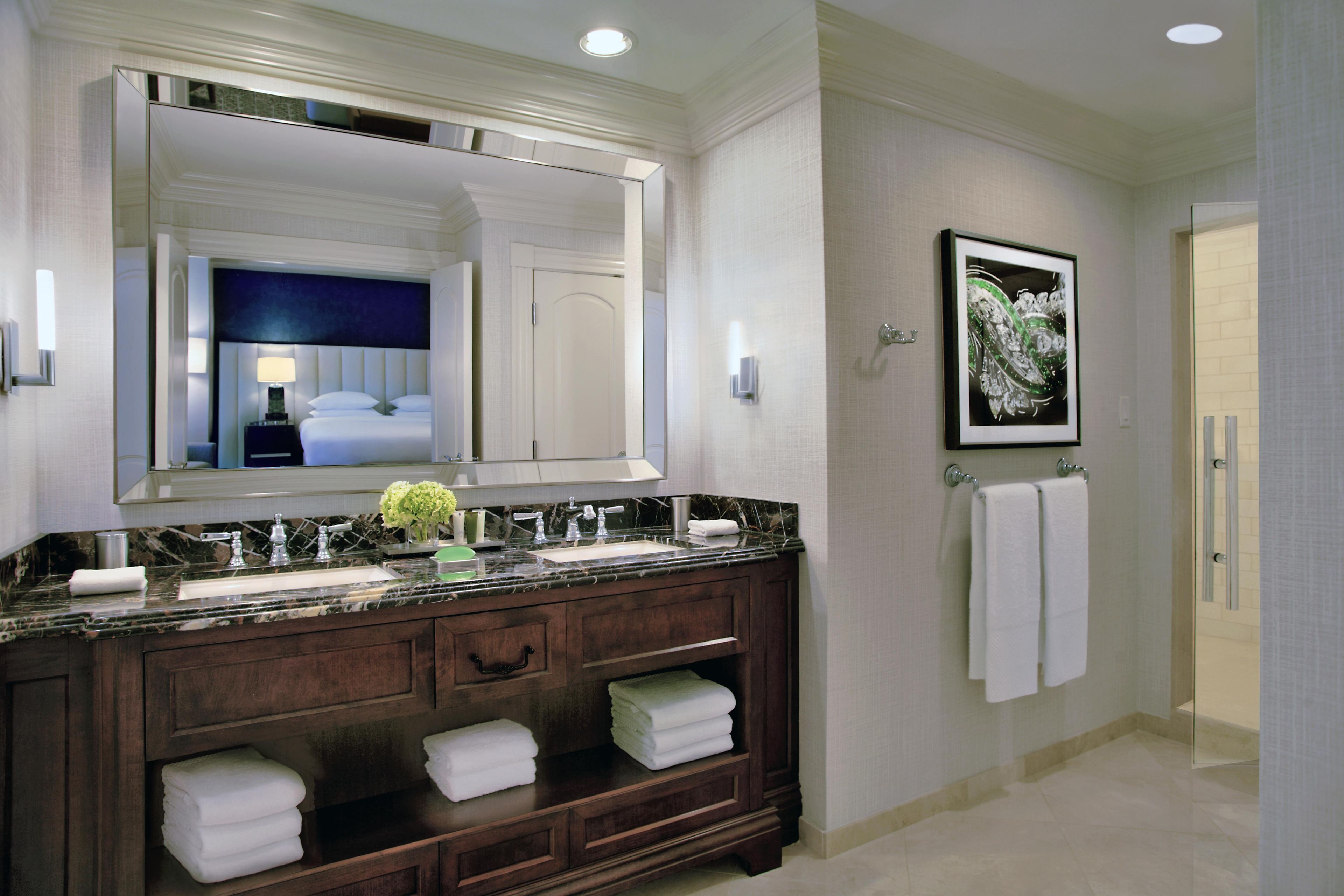 A modern bathroom with a large mirror, dual sinks, a dark wooden vanity, and a framed artwork on the wall.