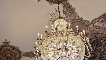 Un candelabro ornamentado con múltiples luces similares a velas, rodeado de elaborados detalles artísticos en el techo.