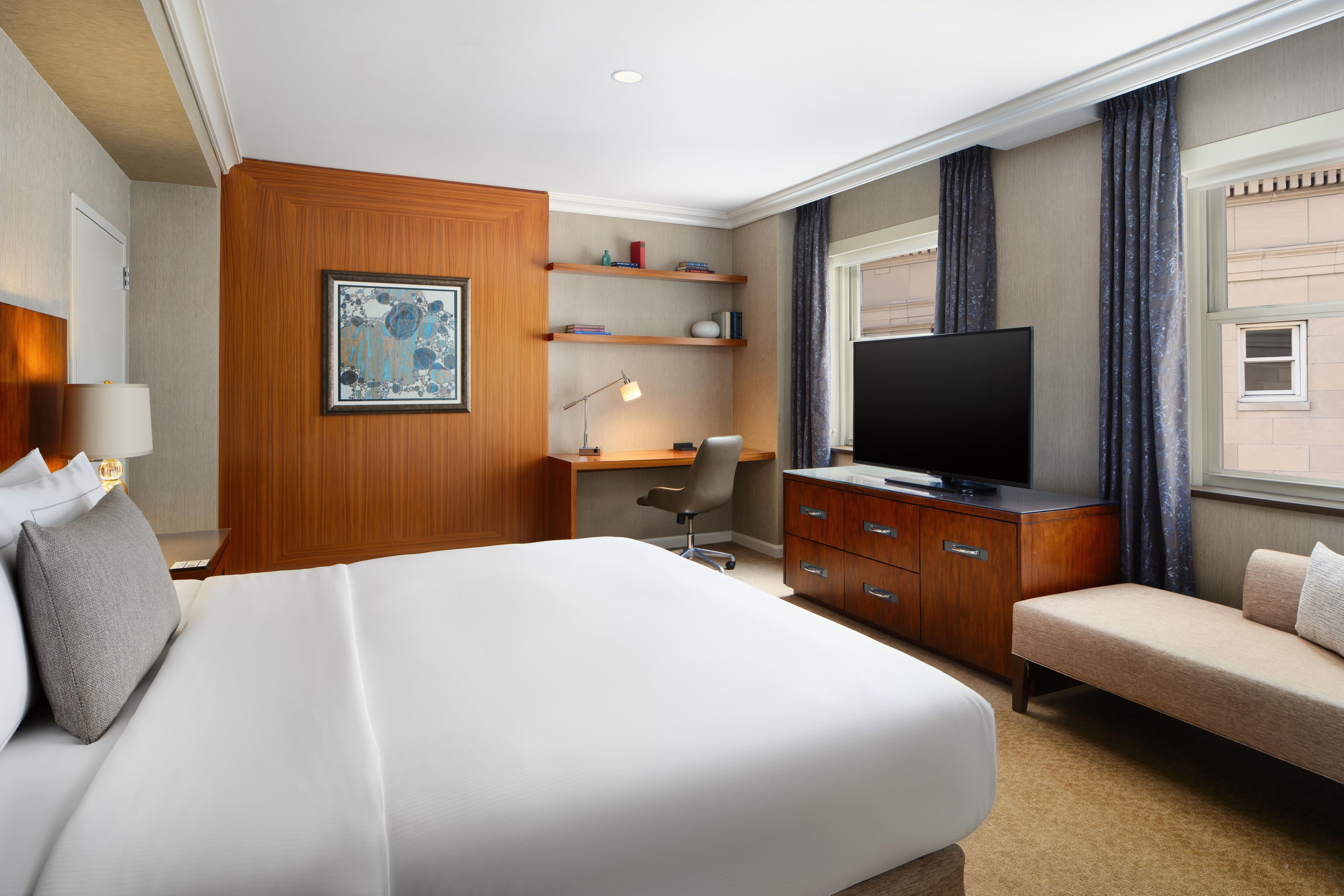 Habitación de hotel con una cama grande, un escritorio, televisor y zona de estar.