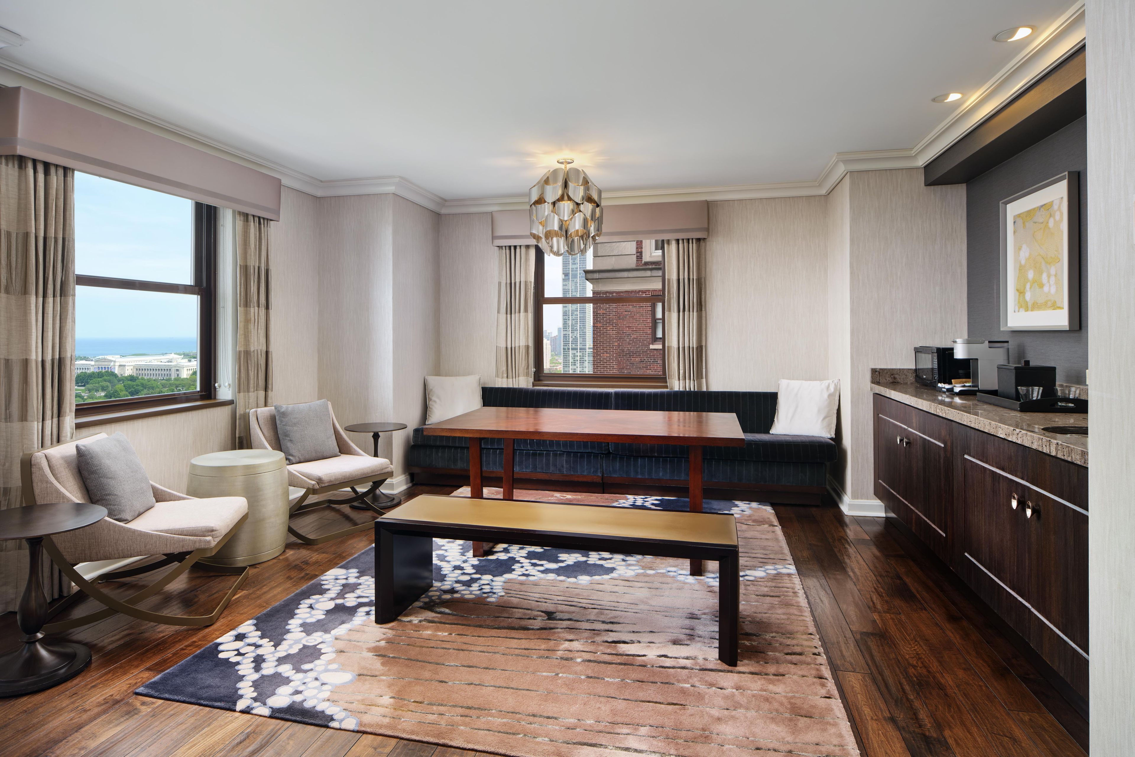 A modern hotel room with a dining area, a sofa, a coffee table, and a view of the cityscape.