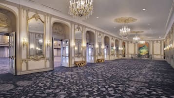 A grand hall with ornate chandeliers, high ceilings, and a patterned carpet.