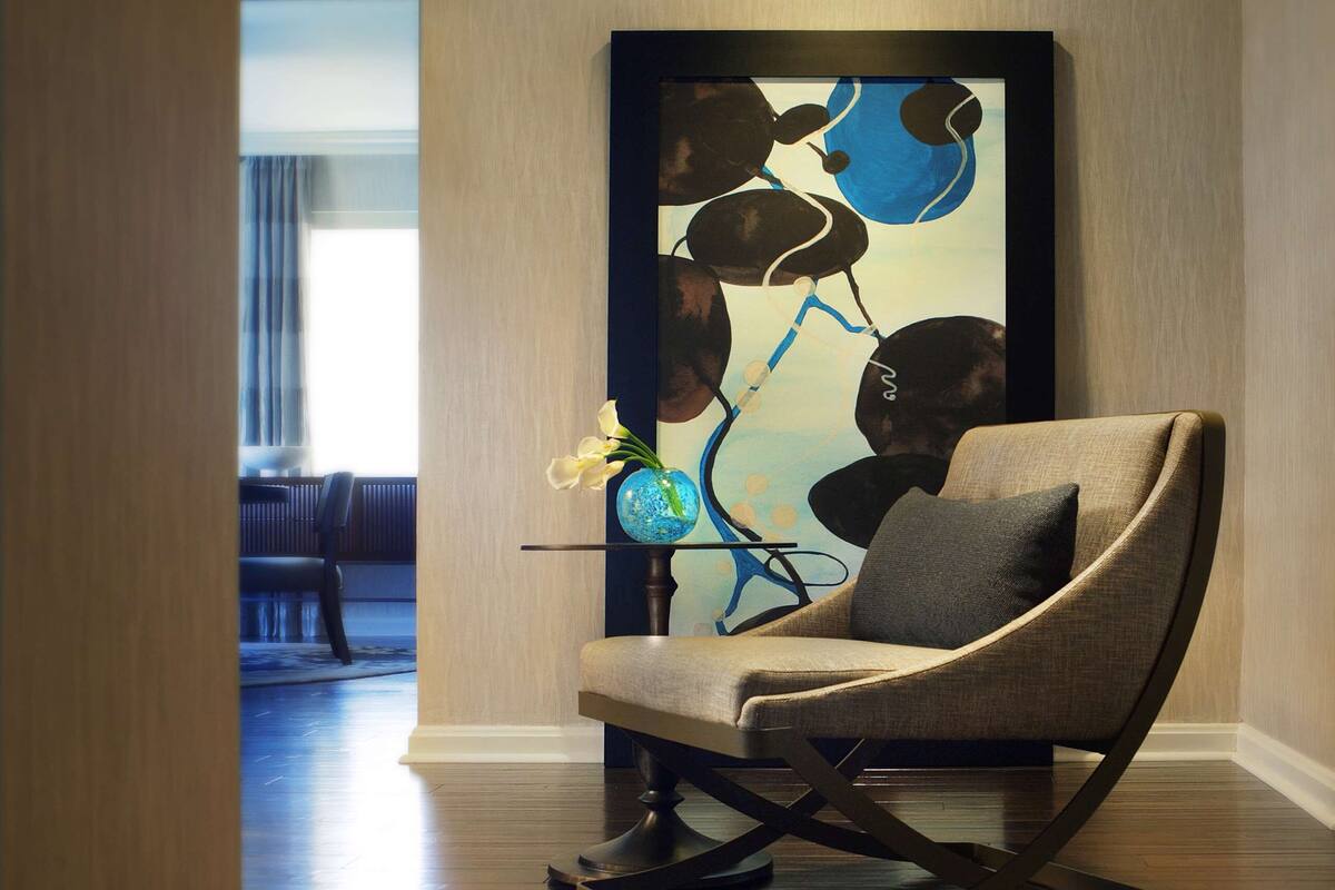 Un interior moderno con una butaca curva tapizada, una mesa de vidrio con un florero y un cuadro abstracto y colorido en la pared.