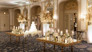 Un salón de baile imponente con candelabros ornamentales, un pastel de bodas de varios niveles como centro de mesa y elegantes arreglos florales sobre las mesas.
