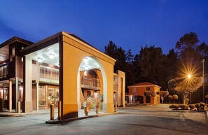 A hotel with a modern design, featuring a prominent archway entrance, a covered outdoor area, and a parking lot. - MHO Inn & Suites (Monmouth Junction)