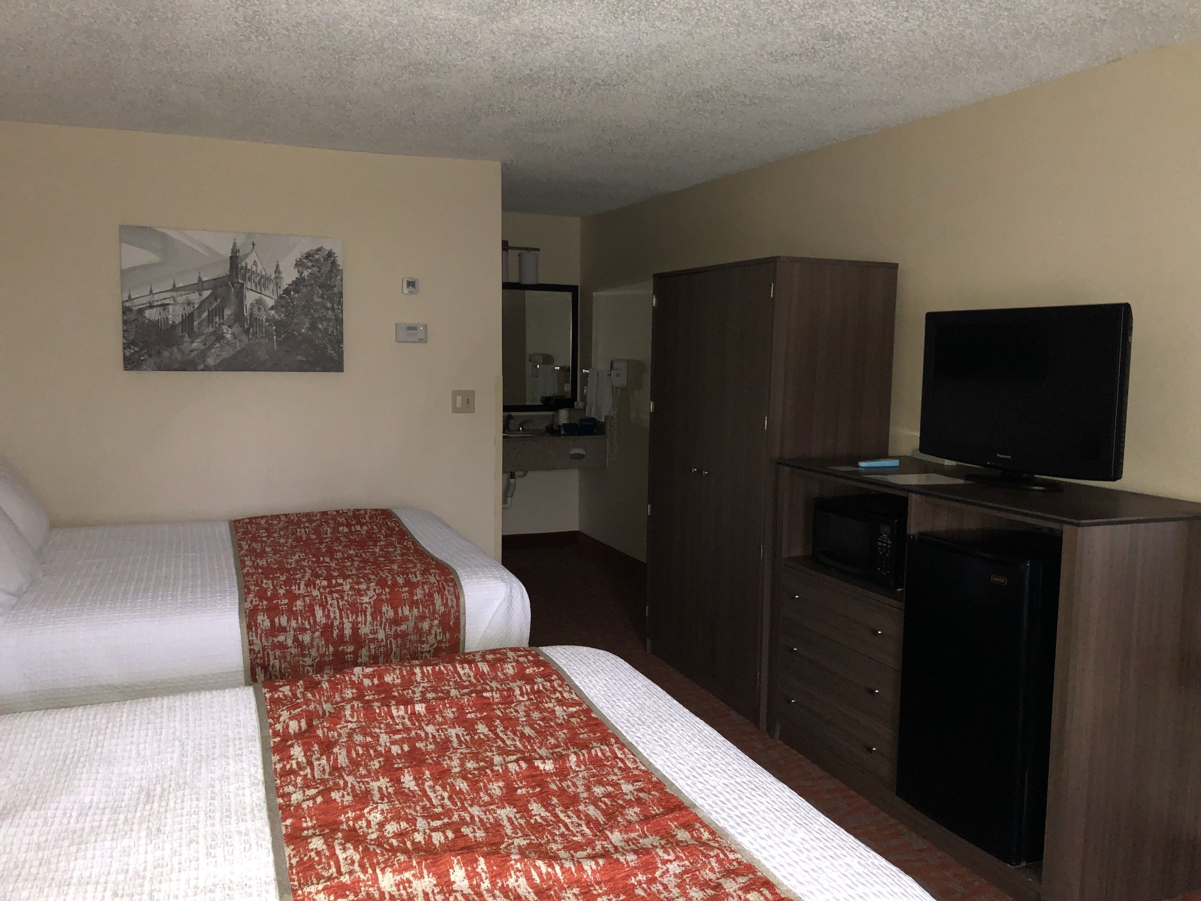 A hotel room with two beds, a television, a wardrobe, and a bathroom visible in the background.