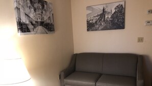 Een woonkamer met een grijze bank, een klein houten tafeltje en twee zwart-wit foto’s aan de muur.