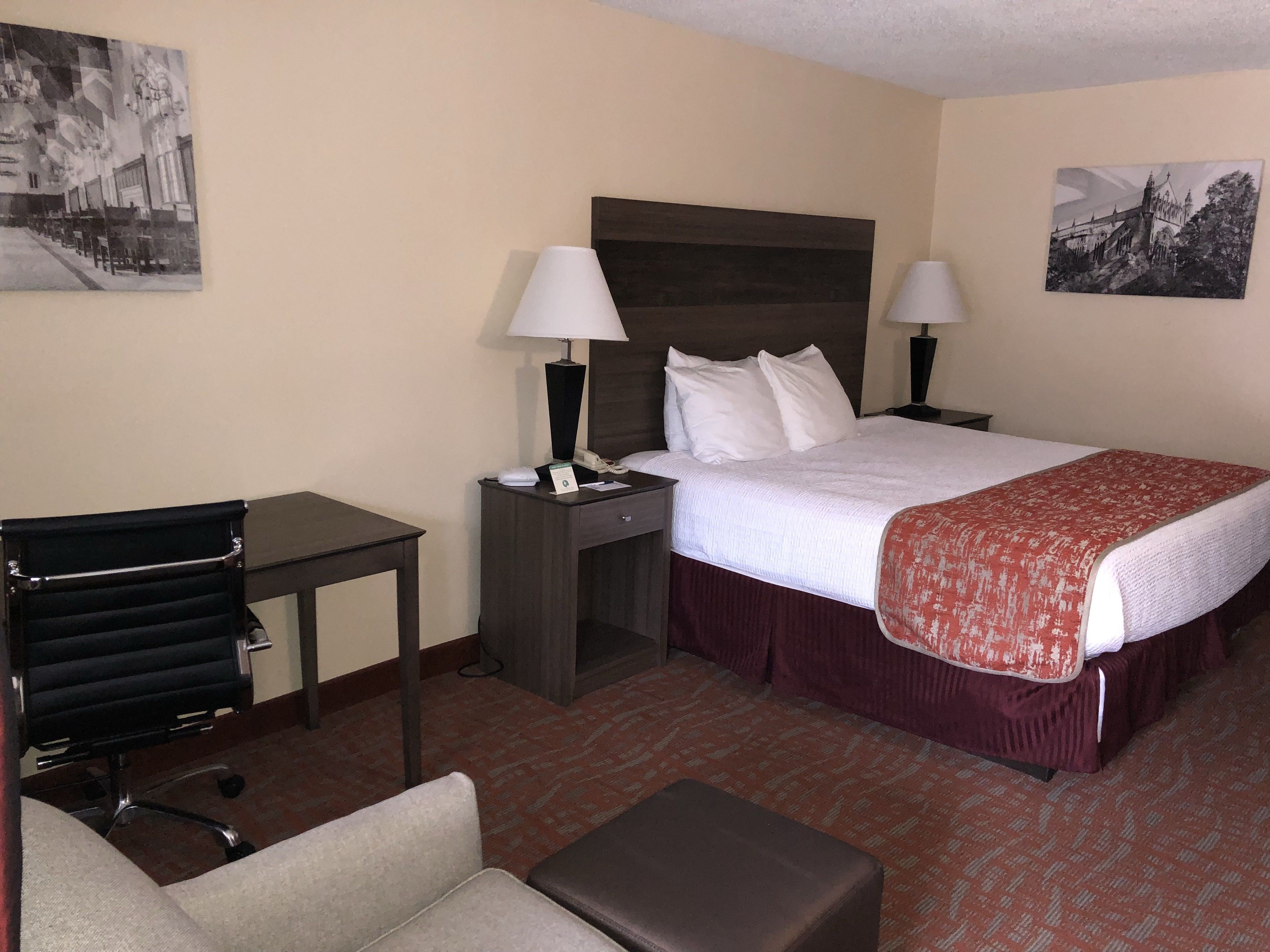 Una habitación de hotel con una cama, dos mesitas de noche con lámparas, un escritorio, una silla y una pequeña mesa.