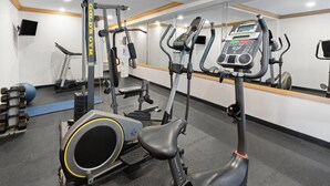 Un gimnasio con máquinas de cardio, equipo de levantamiento de pesas y un espejo grande.