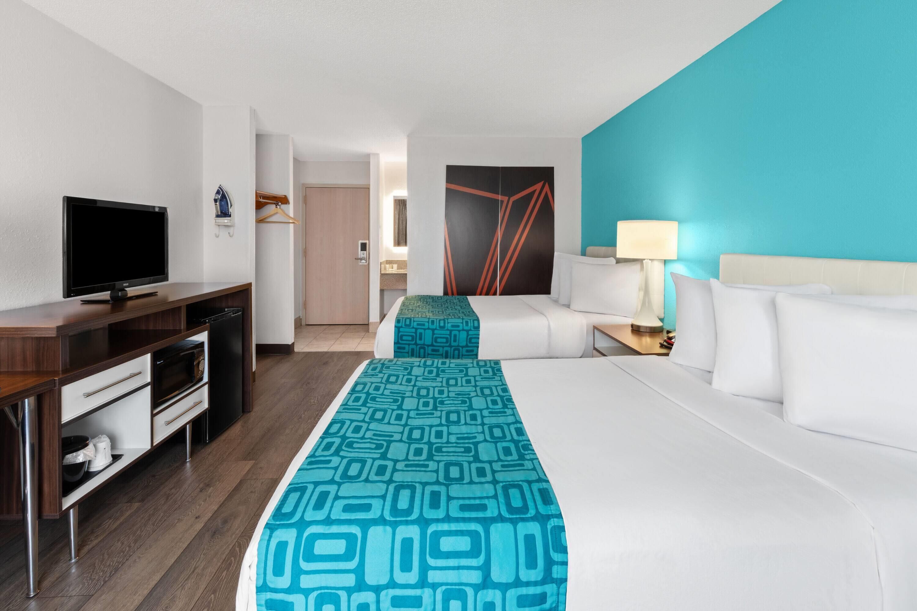 A hotel room with a bed, a desk with a television, a microwave, and a small kitchenette.