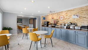 Una cocina moderna con suelo de mármol, sillas amarillas, una mesa blanca y una pared de ladrillo con un cartel de pan.