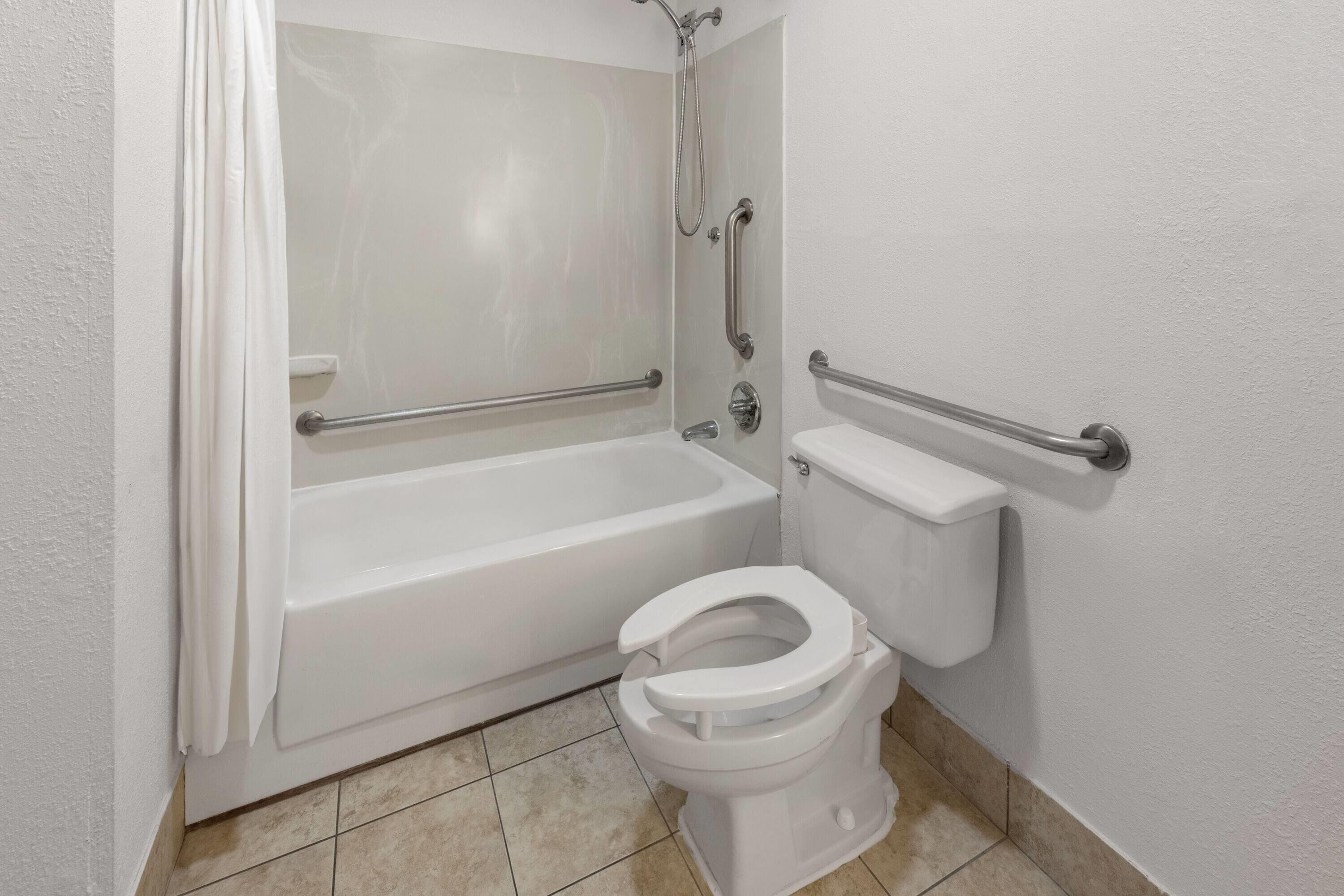 A bathroom with a bathtub, toilet, and grab bars.