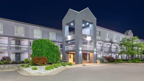 Un hotel de varios pisos con un atrio central, balcones y un jardín delantero ajardinado.