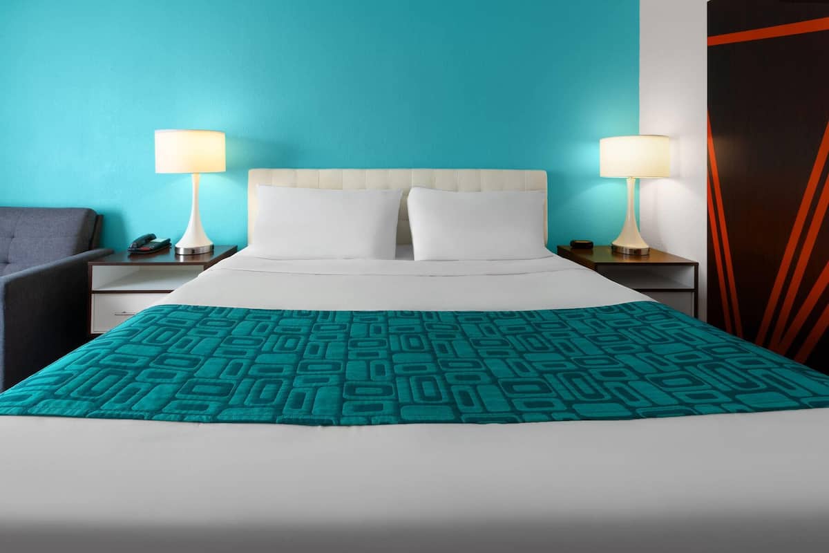 A hotel room with a bed, two bedside tables, a nightstand, a telephone, and a lamp.