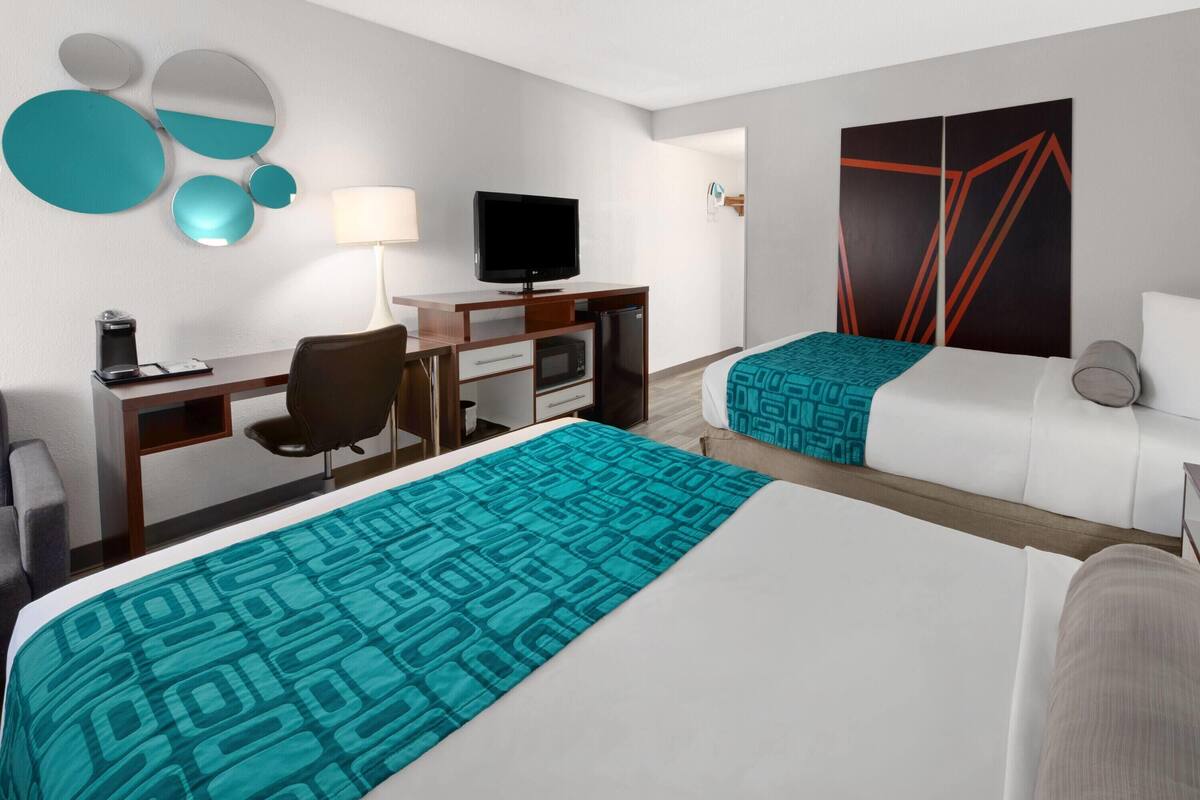 A hotel room with two beds, a desk with a TV, a coffee maker, and a microwave.