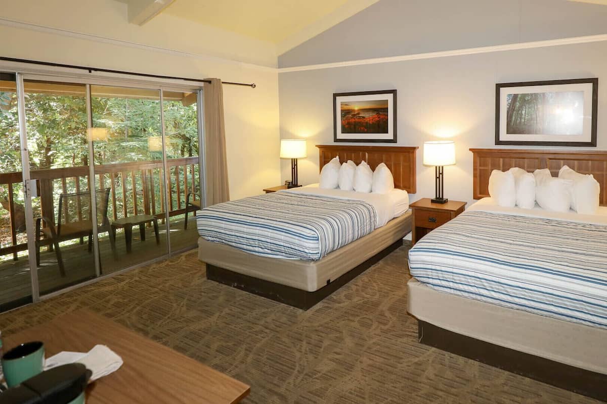 A hotel room with two beds, a balcony, and two framed pictures on the walls.