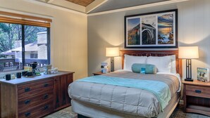 A hotel room with a bed, wooden headboard, two bedside tables with lamps, a dresser, a window with blinds, and a framed picture above the bed. - Big Sur Lodge (Big Sur)