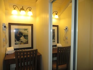 A hotel room with a wooden desk, a framed picture, a hairdryer, and wall-mounted lamps.