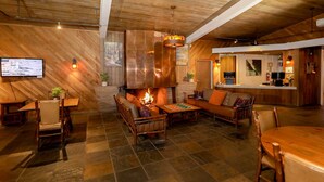 A cozy lounge area with a fireplace, wooden furniture, and a television mounted on the wall. - Big Sur Lodge (Big Sur)