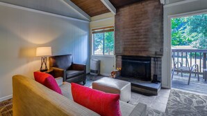 A cozy living room with a fireplace, comfortable seating, and a view of the outdoors. - Big Sur Lodge (Big Sur)