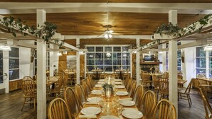 A long dining table set for a meal in a spacious room with wooden flooring and white pillars. - Big Sur Lodge (Big Sur)