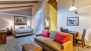 Una habitación de hotel moderna con una cama, un sofá, una mesa de comedor y sillas. Hay dos lámparas en las mesitas de noche y un ventanal con vistas.