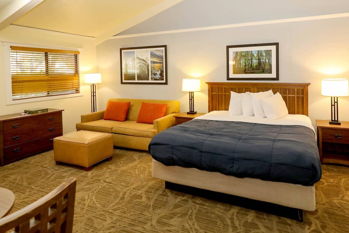 A hotel room with a large bed, a sofa, a wooden dresser, and two bedside tables with lamps.