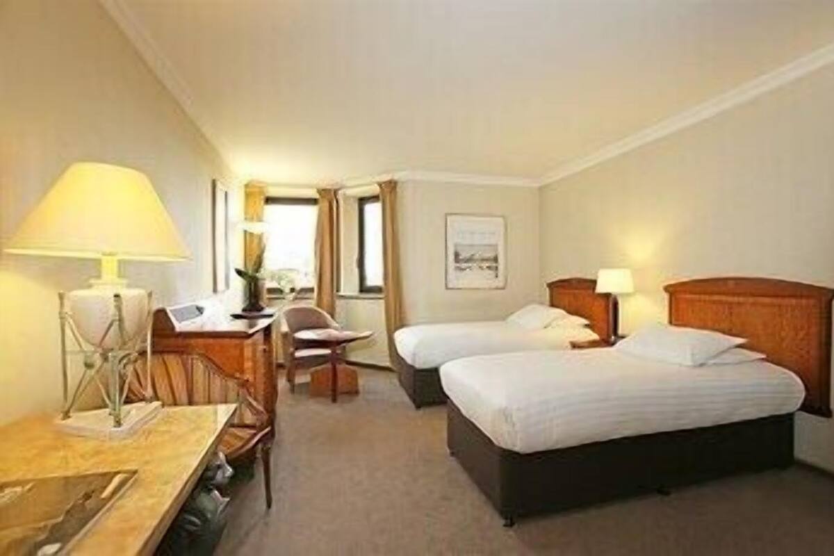 A hotel room with two beds, a desk with a lamp, a chair, and a window.