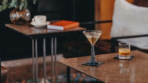 A bar area with a martini glass and a whiskey glass on a granite table, a vase with flowers, and a book on a side table.