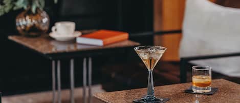 Una zona de bar con una copa de martini y una copa de whisky sobre una mesa de granito, un florero con flores y un libro en una mesita auxiliar.