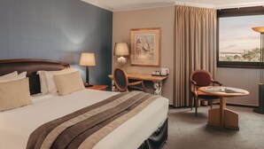 Habitación de hotel con cama, escritorio, silla, lámpara y ventana con cortinas.