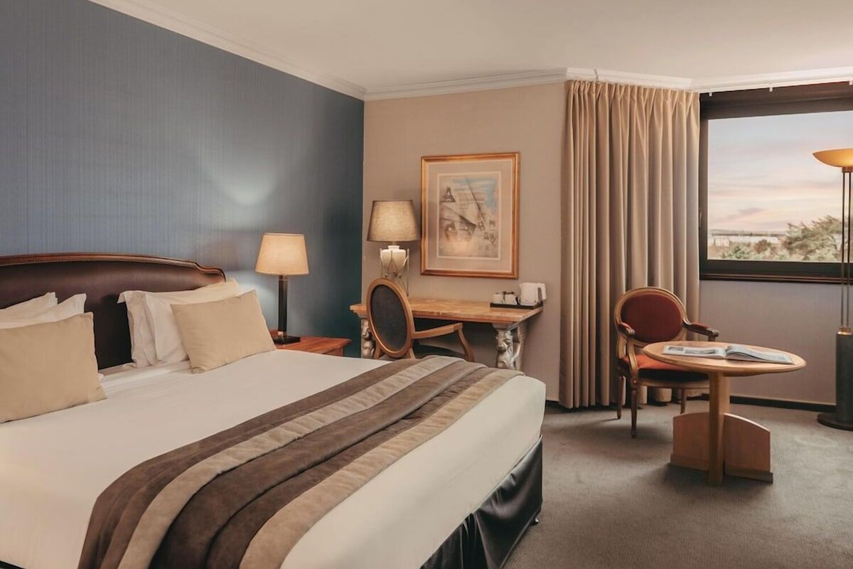 Habitación de hotel con una cama grande, un escritorio, una silla y vistas al exterior.