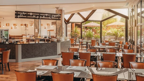 A restaurant with a bar area, multiple tables and chairs, and large windows offering a view of the outdoors.