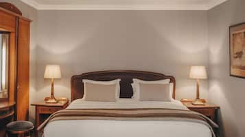 Habitación de hotel ordenada con una cama grande, dos mesitas de noche, una silla y un cuadro en la pared.