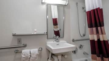 A bathroom with a sink, mirror, shower, and handrails.