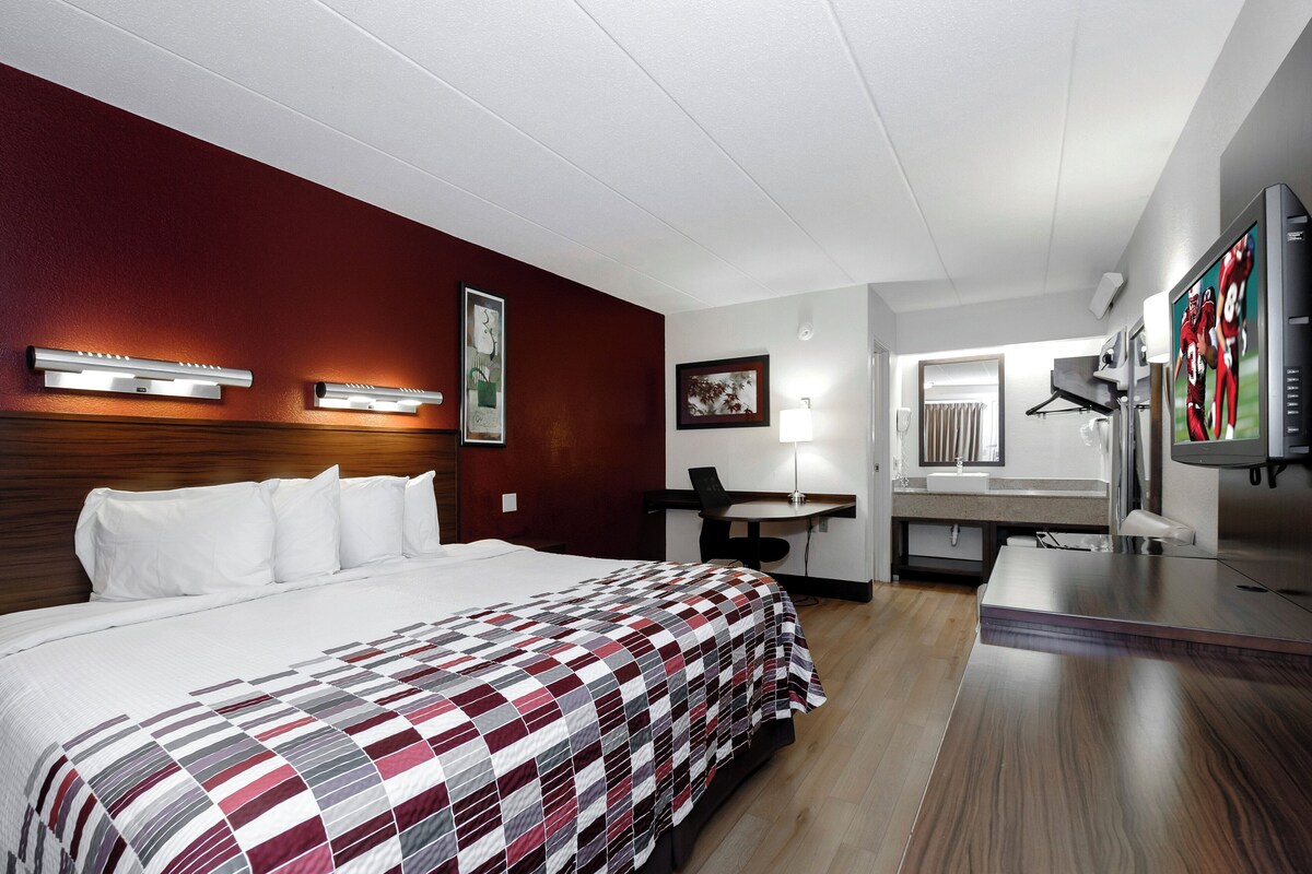 A hotel room with a bed, desk, chair, TV, and a mirror.