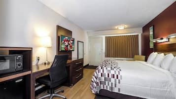 A hotel room with a bed, desk, chair, microwave, and artwork on the wall.